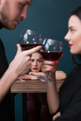 Sad left alone female in bar. Jealousy backdrop. Cheating relationships. Unhappy lonely woman in focus on blue background, loneliness concept