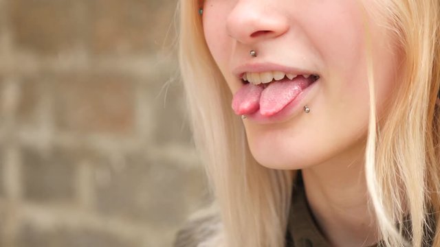 bodimodification, portrait of a girl with face piercings and tunnels in the ears. a girl with a split tongue. shows the language. 4k, slow-motion shooting, copying space