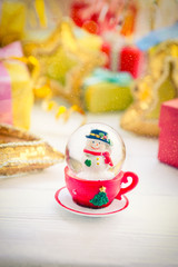 Colorful Merry Christmas background. Snowball with Snowman inside, snow flake is falling down. New year Gifts and decoration. Vintage postcard. Space for text. Selective focus