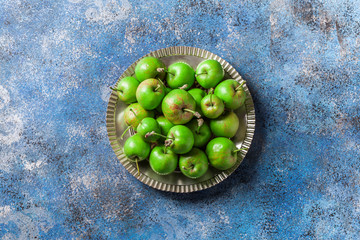 Green organic apples overhead on silver plate and painted blue background in studio