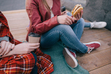 Burger and coffee in hands of young women. Favorite junk food close up. Unhealthy meals and hurry...