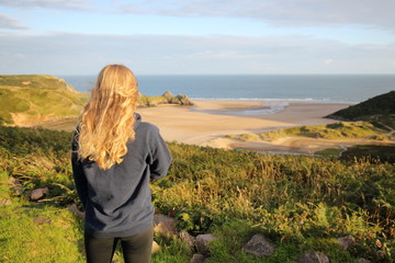 rear view of young blonde girl overlooking a beach panorama at Three Cliffs Bay in Wales, UK