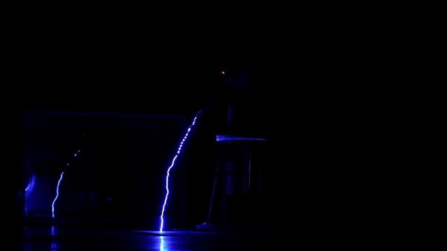 Performance on stage at the festival of science. A scientist in a special suit controls the electrical discharges in the dark. Slow motion