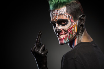 Side view if a man with colored skull makeup showing long finger. Face art, man with zombie face.