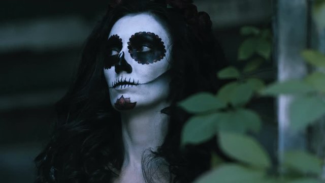 The Mexican Day of the Dead. The young woman with scary skull halloween make-up holding in the arms a pumpkin with a burning candle. 4K