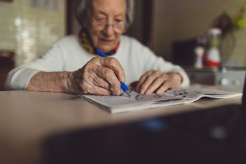 Old woman solving crossword puzzles in the kitchen