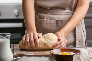 Female chef kneading dough on wooden board at kitchen