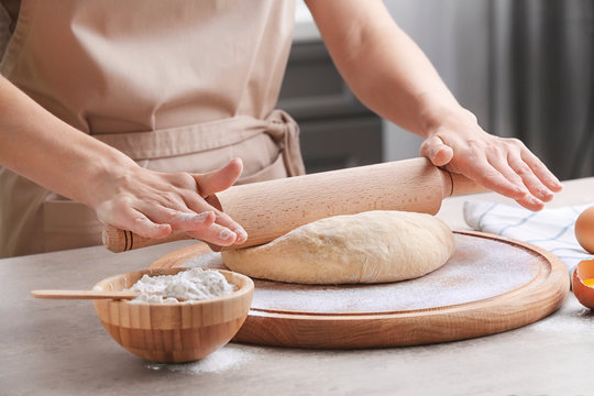 Female chef rolling dough on wooden board at kitchen