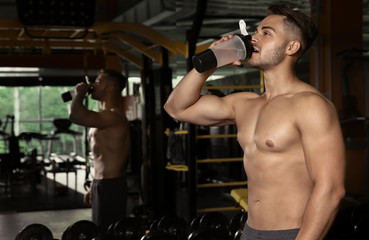 Sporty young man drinking water in gym