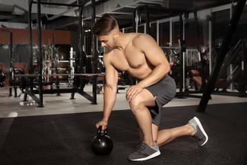 Young sporty man doing exercise with kettlebell in gym