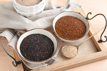 Bowls with different quinoa seeds on wooden tray