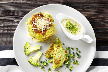 Plate with delicious broccoli pancakes and sauce on wooden background