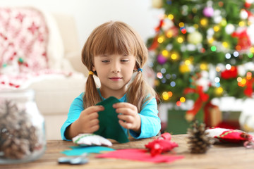 Naklejka premium Little girl making felt Christmas fir tree at table