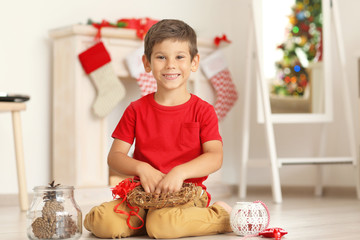 Cute boy decorating Christmas wreath on floor