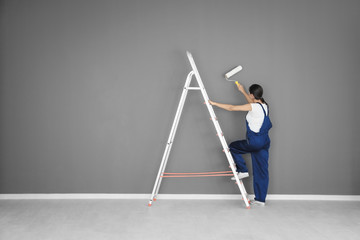 Young female decorator painting wall in room