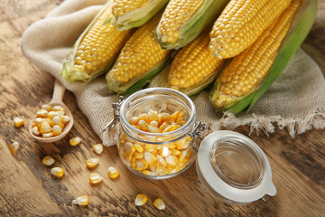 Corn cobs and glass jar with kernels on wooden table