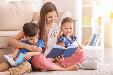Fototapeta premium Young woman and her little children reading books at home