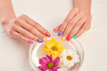 Manicured hands on glass bowl with water. Young woman hands with colorful nails receiving spa treatment. Aroma therapy for female hands.