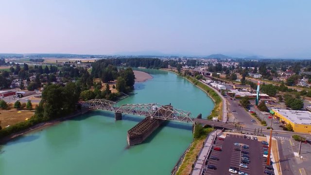 Aerial of a bridge with moving traffic crossing a river with vast rural cityscape background on bright, hot and sunny summer day