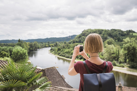 Young blond woman taking a landscape picture on her phone