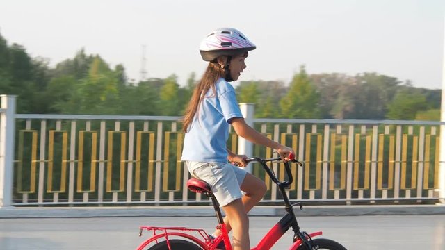 The child is riding a scooter. A little girl in a helmet is riding a scooter.