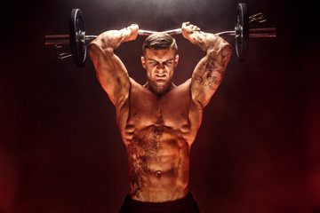 Portrait of muscular man lifting dumbbell in red smoke. Studio shot. Exercise for triceps....