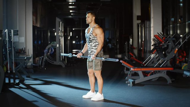 Handsome sportsman trains his hands and shoulders with barbell weight in gym