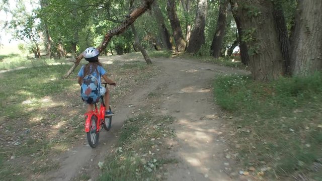 Child with a bicycle in nature. A little girl in a helmet is riding a bicycle in the forest.