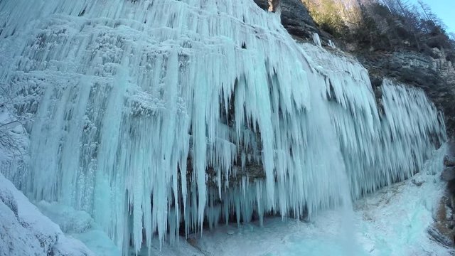 CLOSE UP Stunning frozen waterfall icicles on rocky mountain cliff on winter day. Winter cascade frozen into numerous white icicles. Waterfall falling past hundreds of icicles. Winter wonderland