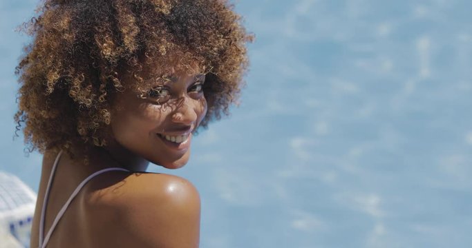 Portrait of charming young woman in swimming suit relaxing in resort pool and posing camera smiling happily in sunlight.