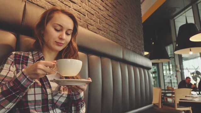 Woman drinking coffee in a cafe, 4K Slow Motion 120 fps. Stabilazed dolly shot. Young beautiful calm woman enjoying a cup of hot coffee in the restaurant. Relaxed morning breakfast in a city. 