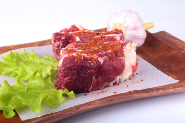 Raw beef edges, lettuce leaf, garlic, pepper grinder and spices on wooden desk isolated on white background from above and copy space. ready for cooking.