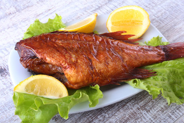 Smoked fish and lemon on green lettuce leaves on Wooden cutting board isolated on white background.
