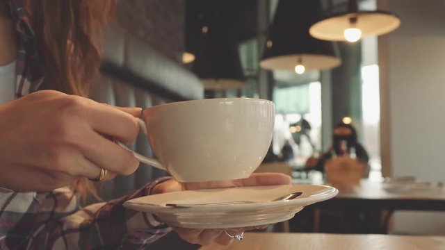 Female hand picking up a cup of coffee, 4K Slow Motion 120 fps. Stabilazed dolly shot. Unrecognizable woman drinking coffee in a cafe, close up on a cup. Brunch, breakfast or lunch out in the city.  