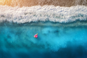 Aerial view of slim woman swimming on the pink swim ring in the transparent turquoise sea in Oludeniz,Turkey. Summer seascape with girl, beautiful waves, blue water in sunny day. Top view from drone - obrazy, fototapety, plakaty
