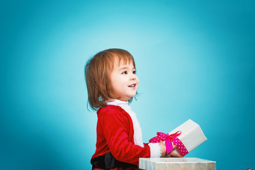 Happy toddler girl in a Santa costume with a gift box
