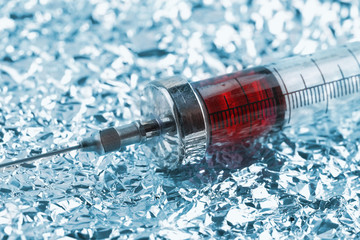 Old filled syringe on the crumpled metallic paper