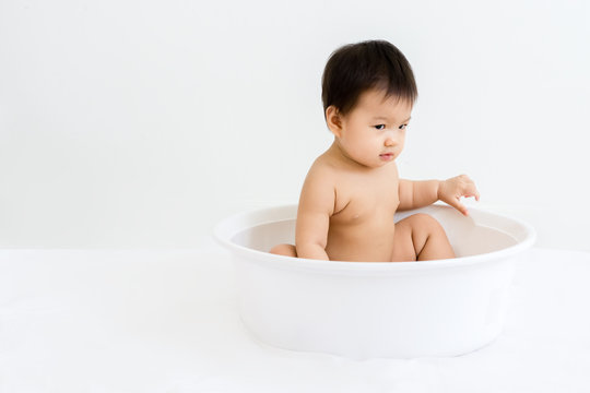 Portrait of adorable baby sitting in the basin for shower, indoors