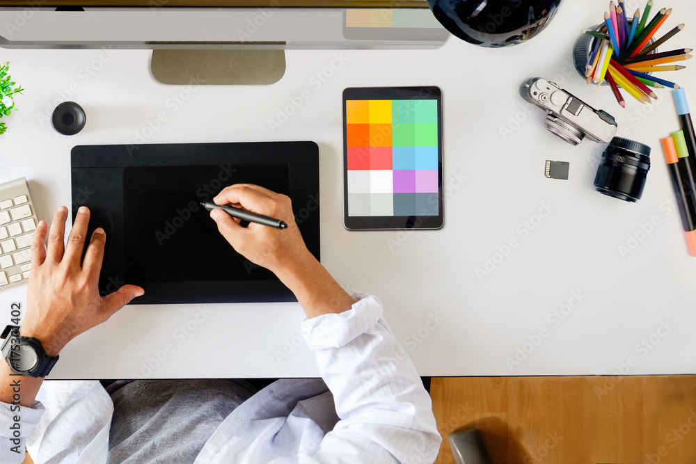 Poster designer drawing on digital tablet at workspace top view with essential elements on white table.