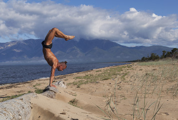  young strong man doing yoga on the shore of a mountain lake,  stand on his hands