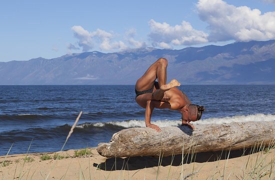  young strong man is practicing yoga on the shore of a mountain lake,
lower arm rest and deep spine twisting