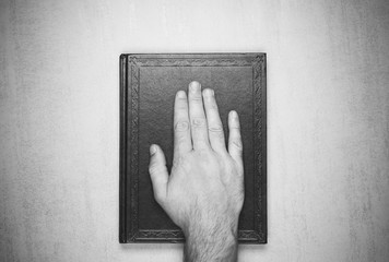 mans hand on the book, the oath on the Bible. top view closeup. black and white photo