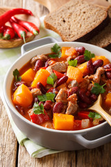 Stewed pumpkin with beans, meat, tomatoes and chili pepper closeup in a pot. vertical