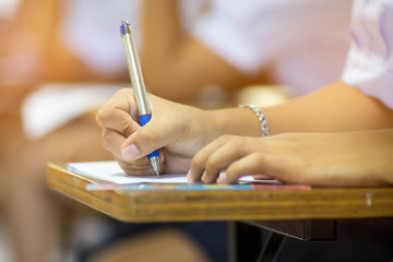 Closeup to hand of student  holding pen and taking exam in classroom with stress for education test .