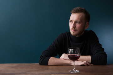 Depressed young man in bar. Sad thoughtful male on blue background with free space, melancholic mood with red wine. Troubles in life, unlucky date