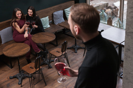 Female seduction. Gossips about male. Flirty women in bar in focus on background, unrecognizable man with wine, flirtation concept