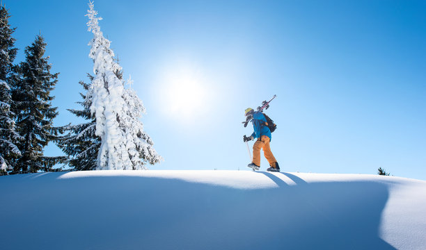 Male skier walking on top of the mountain with his skis on his shoulder on a sunny winter day sunlight nature recreation skiing downhill lifestyle sportive concept