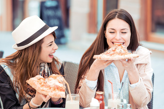 Two cheerful girls eating pizza in cafe