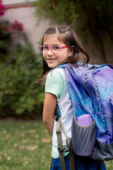 A young girl with pink glasses is excited and nervous for her first day of school.