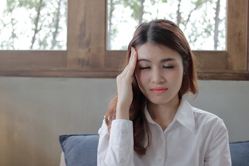 Portrait of stressed young Asian woman close her eyes and touching head in home.